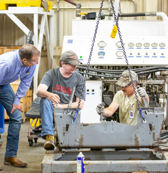 A photo of three Steffes employees assembling an attachment for a contract manufacturing partner on the factory floor