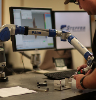 A photo of a Steffes engineer working with a robot to manufacture a stainless steel product