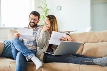 Two satisfied Steffes ETS product owners relax on a couch while they review a bill from their power provider.