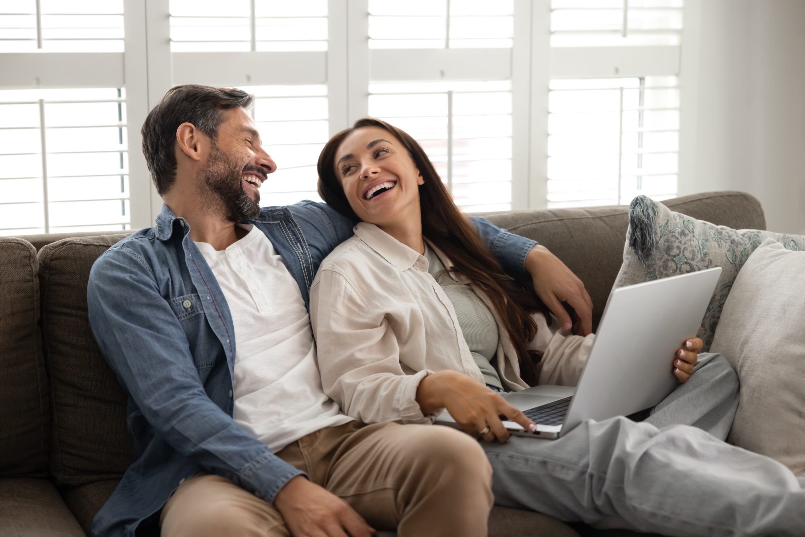 A couple sitting on the couch with a laptop, looking at Steffes's residential heating systems website page.